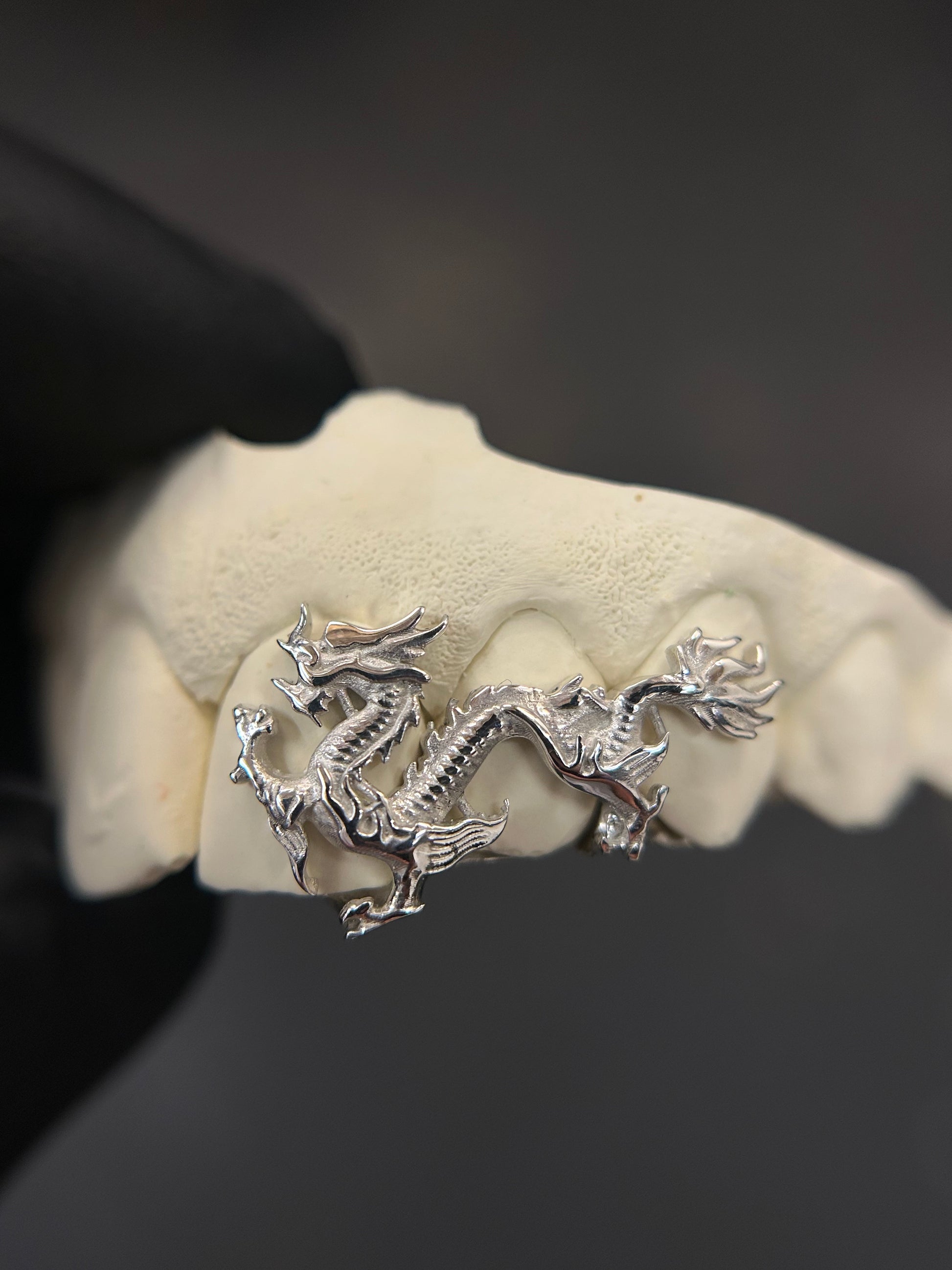 Silver dragon pendant held by a gloved hand against a dark background